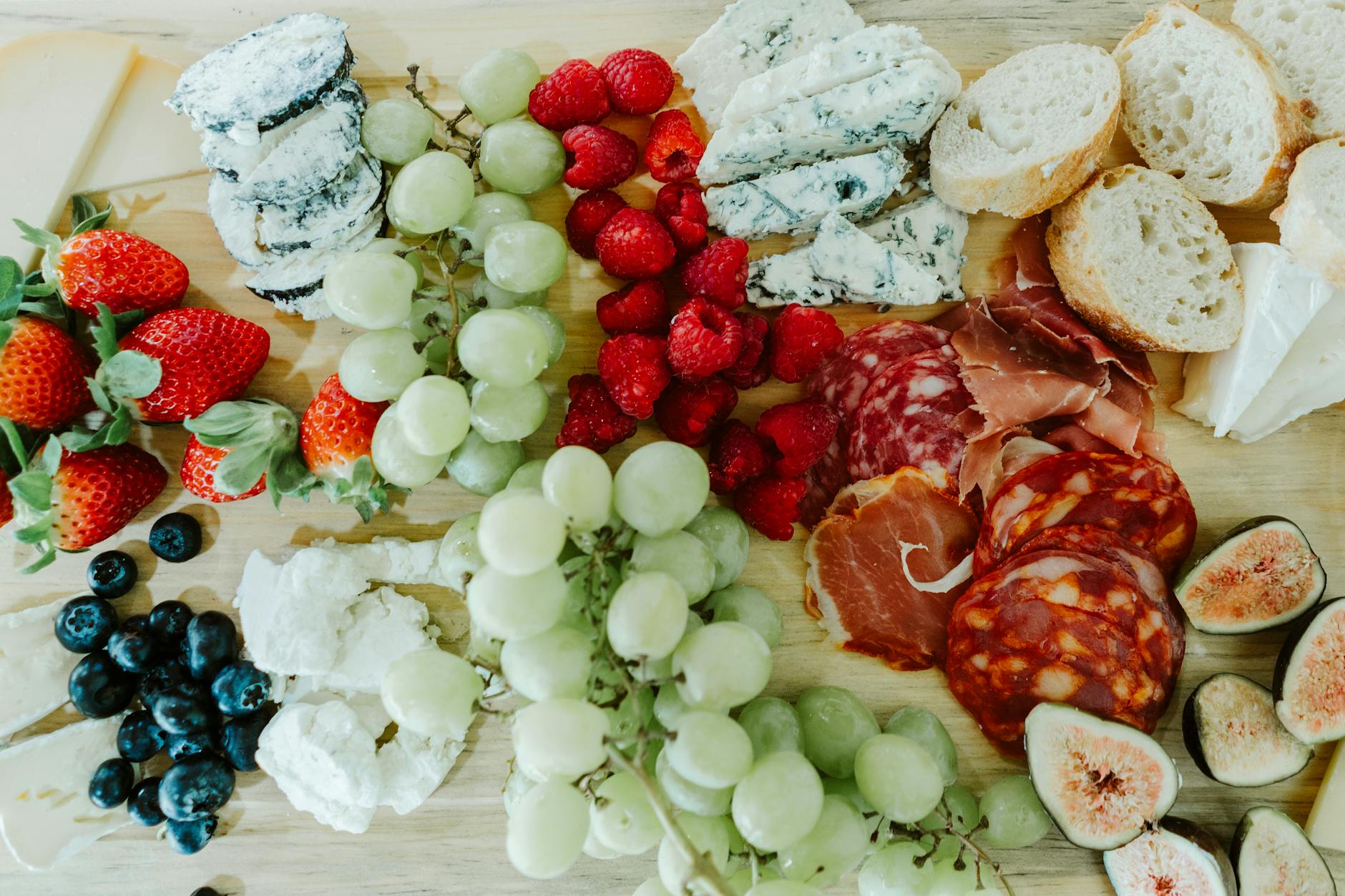 Deska przekąsek z serami, wędlinami i świeżymi owocami na drewnianym blacie