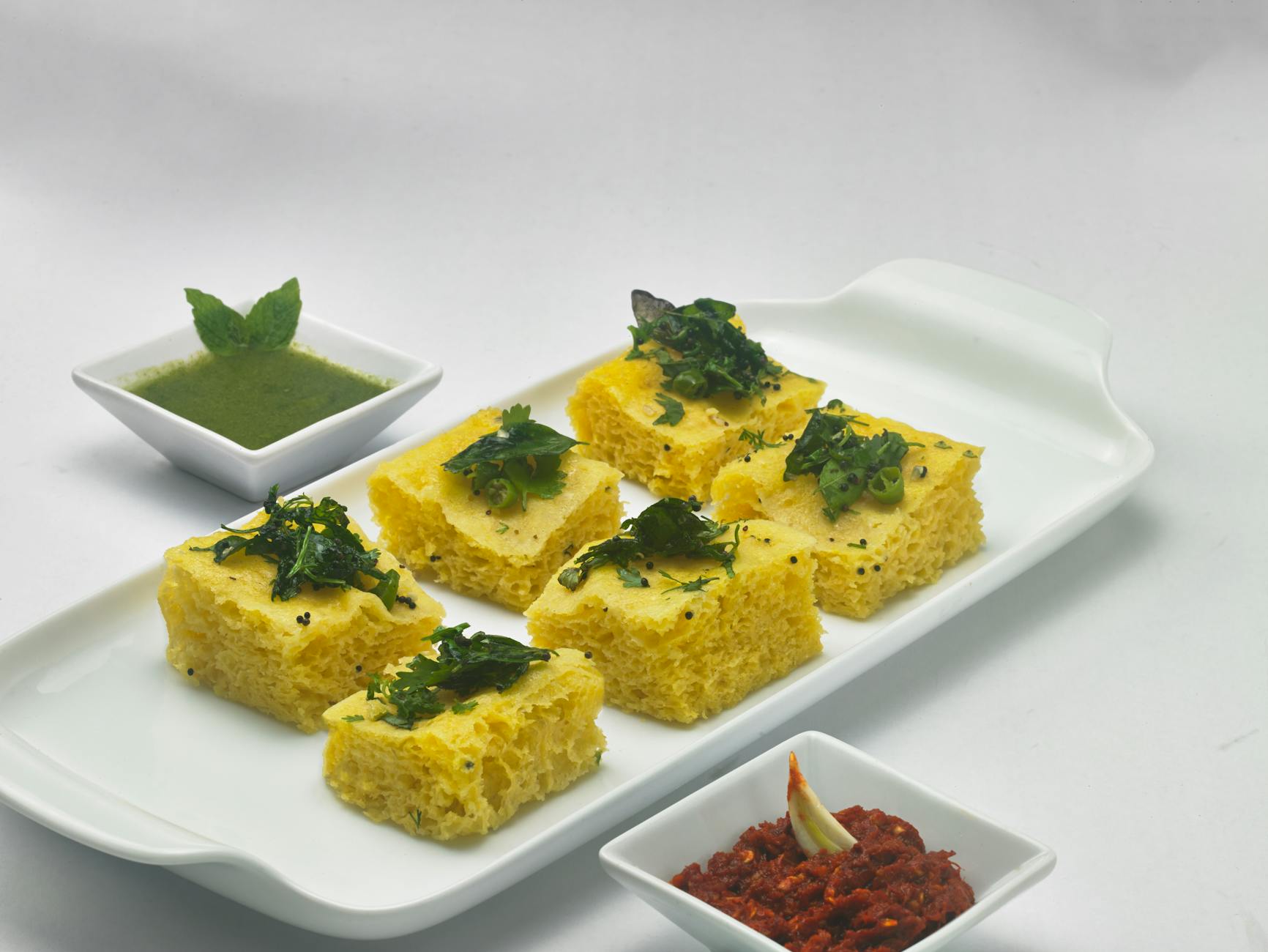 Indyjskie dhokla na białej paterze z dwoma rodzajami chutney