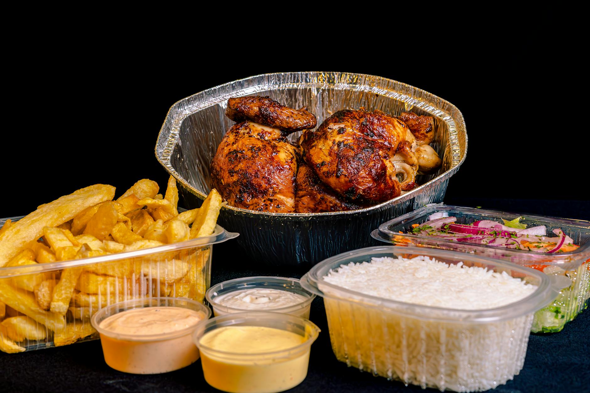 Kurczak z rożna z frytkami, ryżem, sałatką i sosami na talerzu