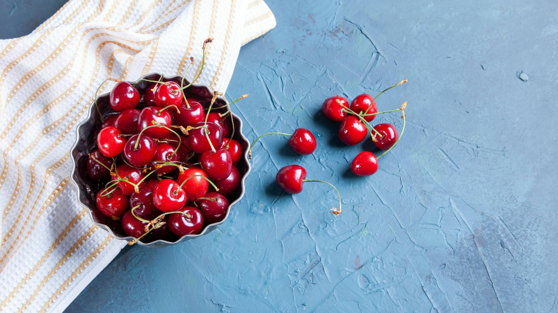 Świeże czerwone czereśnie w rustykalnym naczyniu na niebieskim tle