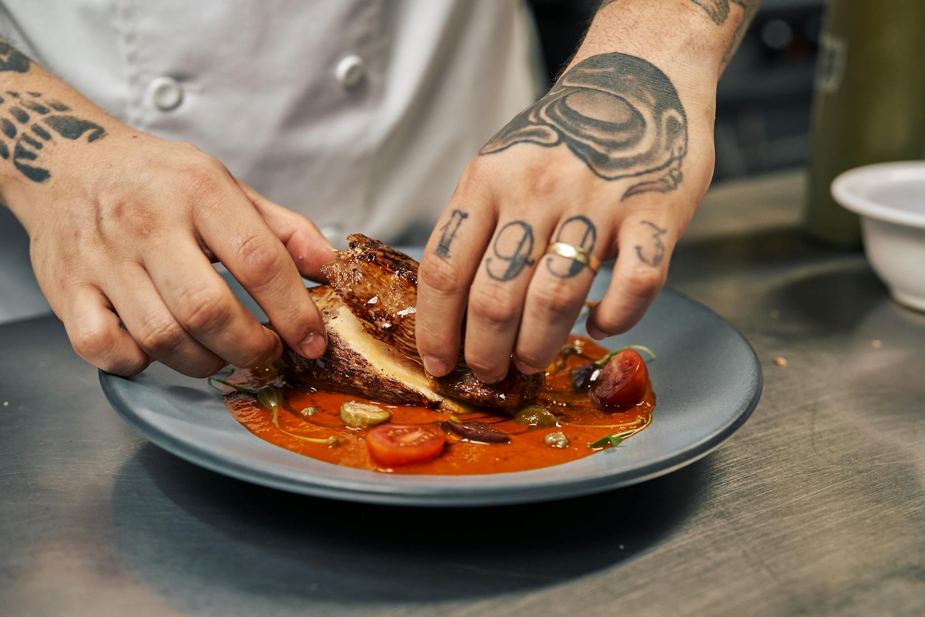 Szef kuchni układa na talerzu danie z kurczakiem i pomidorami
