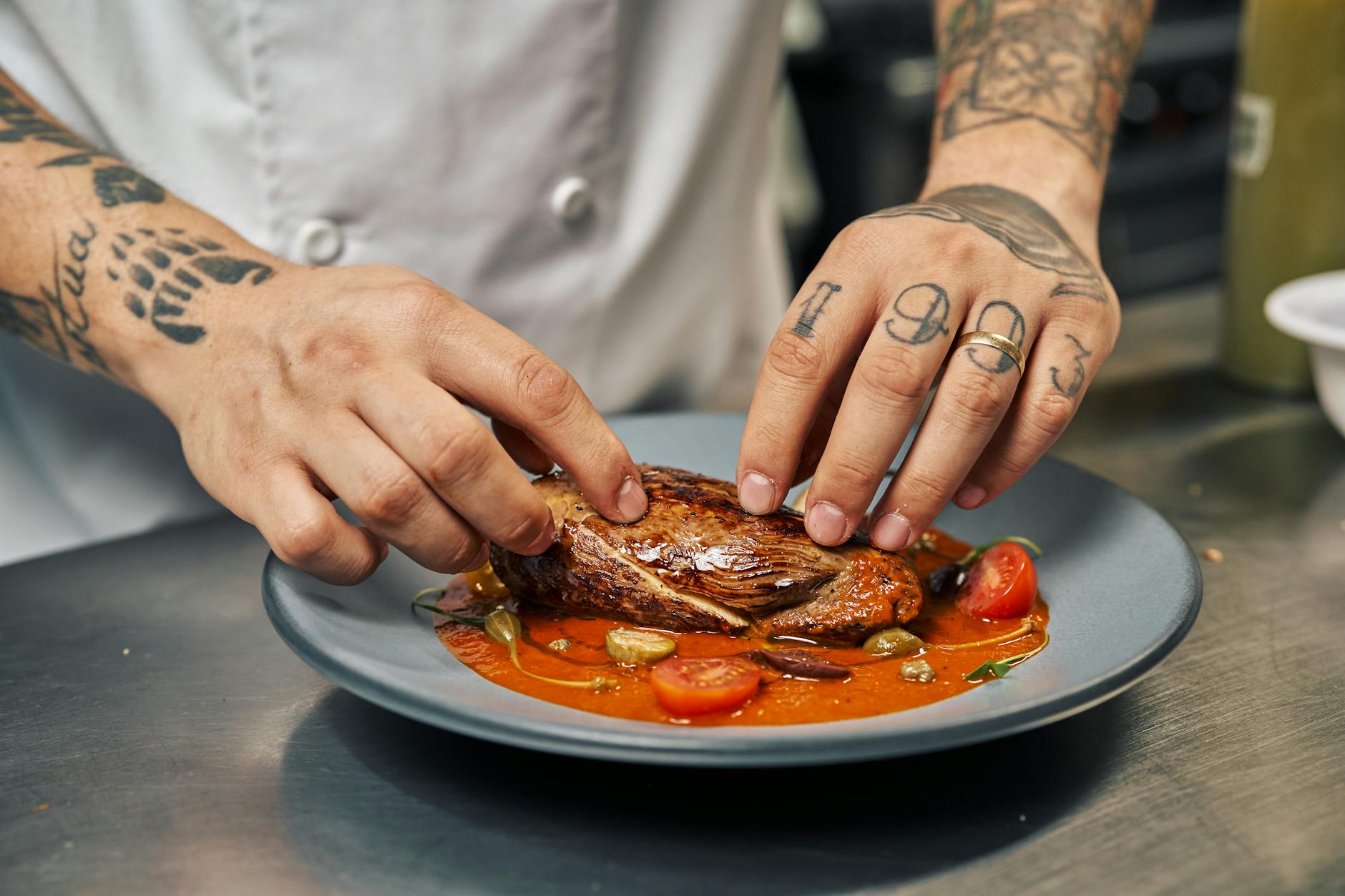 Tatuażowany kucharz podaje stek z dodatkami na kolorowym talerzu