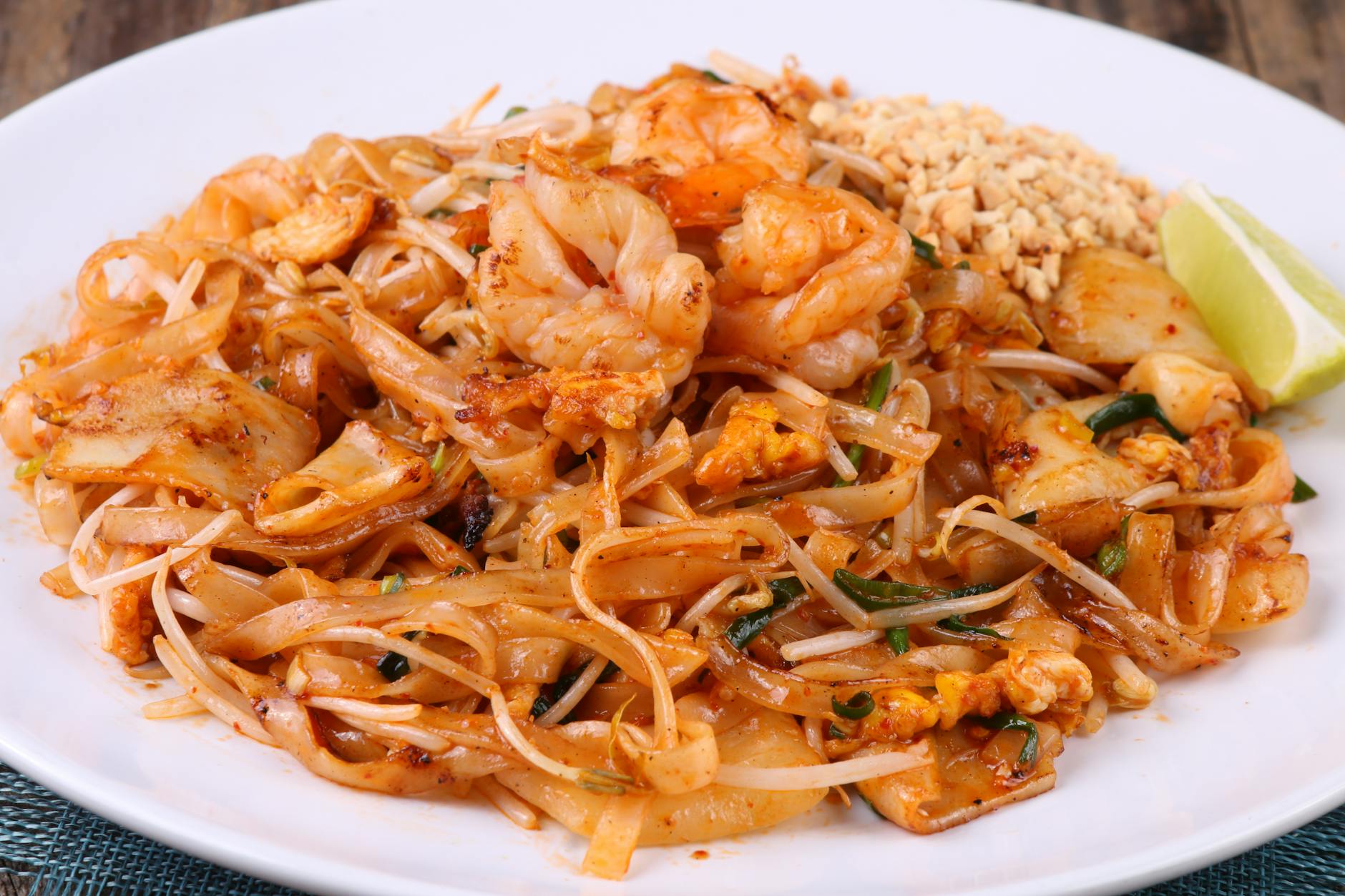 Zbliżenie na krewetkowe pad thai z limonką i orzeszkami na białym talerzu
