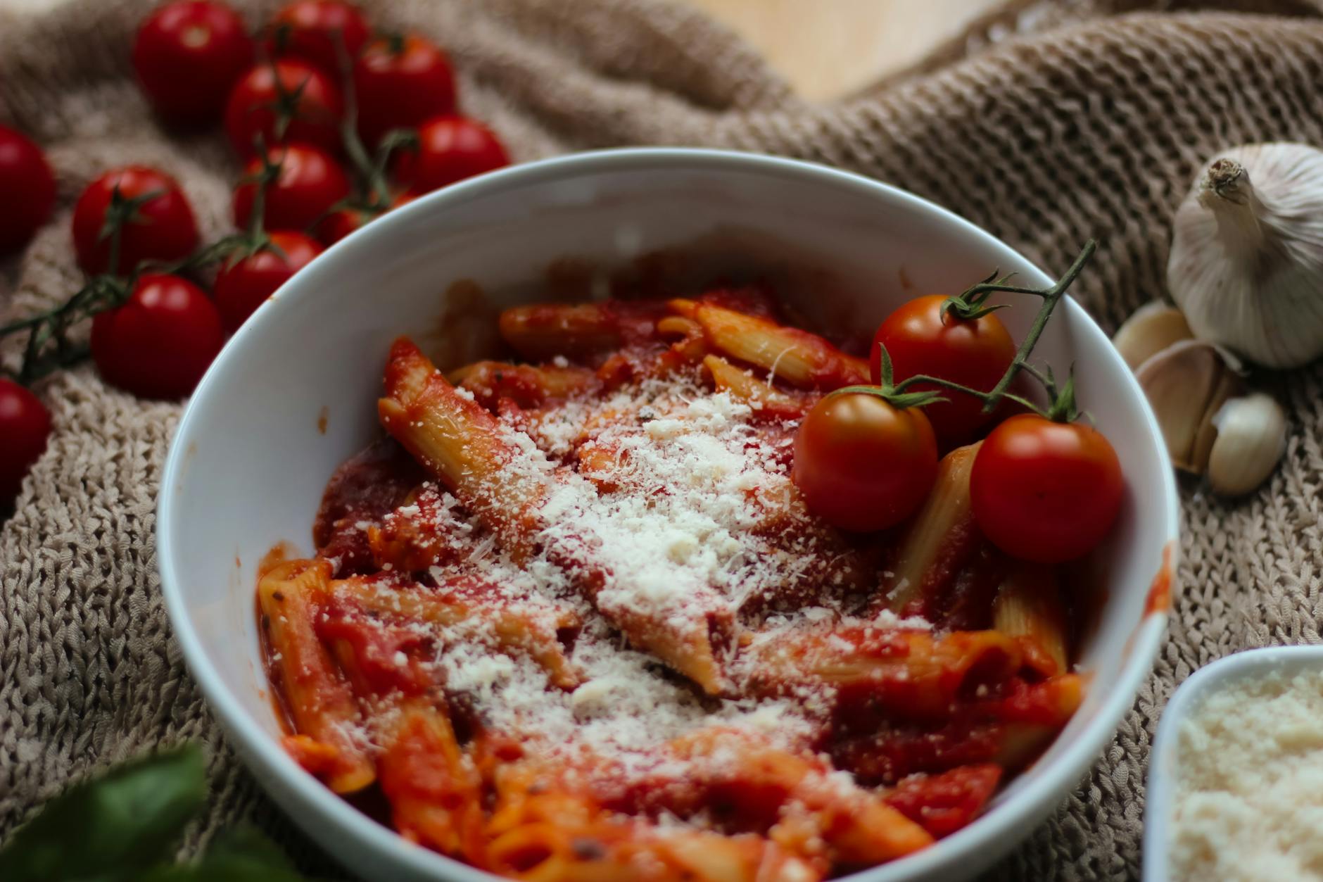 Szybki makaron z pomidorami, czosnkiem i bazylią jak we Włoszech Makaron penne w sosie pomidorowym z parmezanem na talerzu
