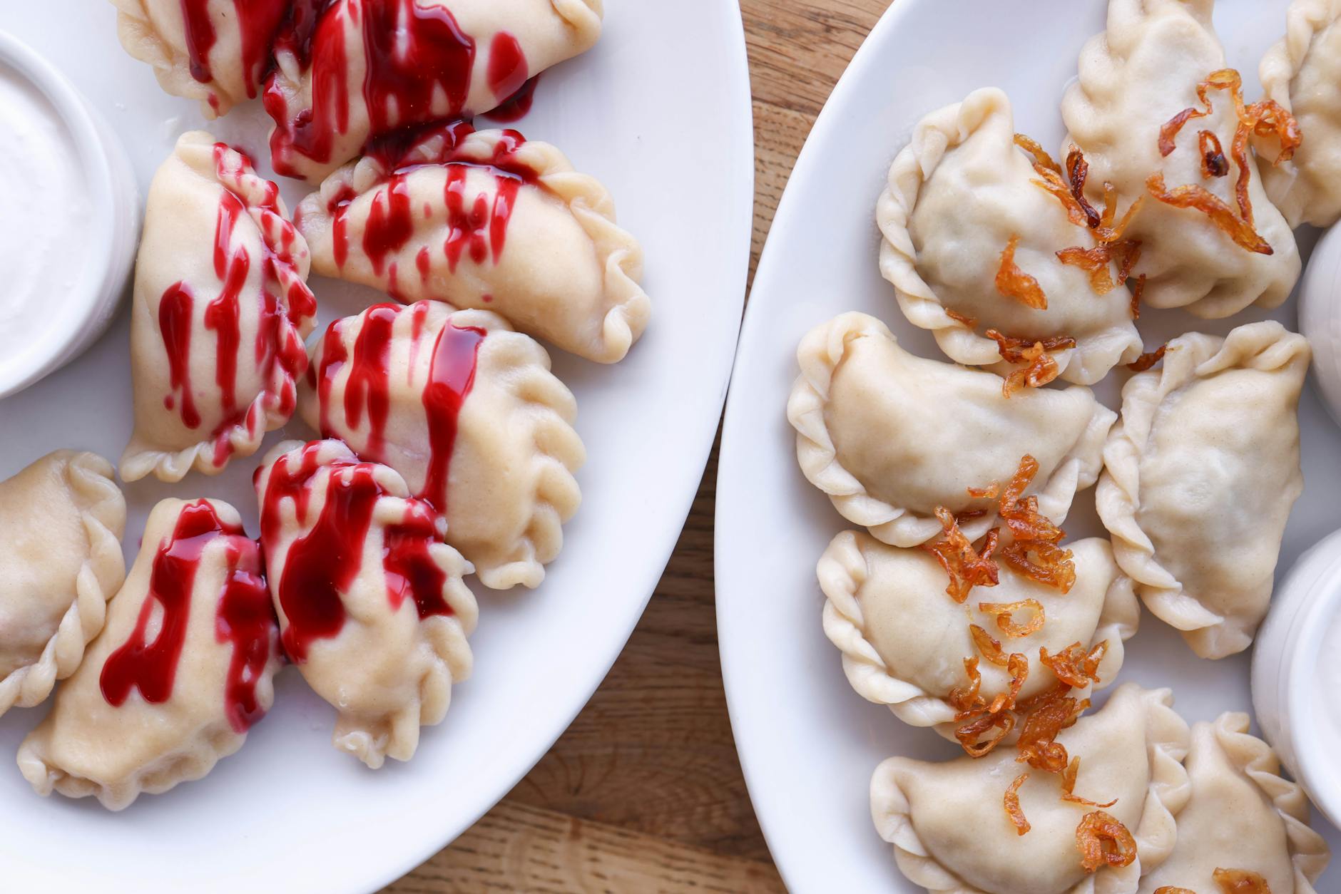 Pierogi na białych talerzach z sosem truskawkowym i prażoną cebulką