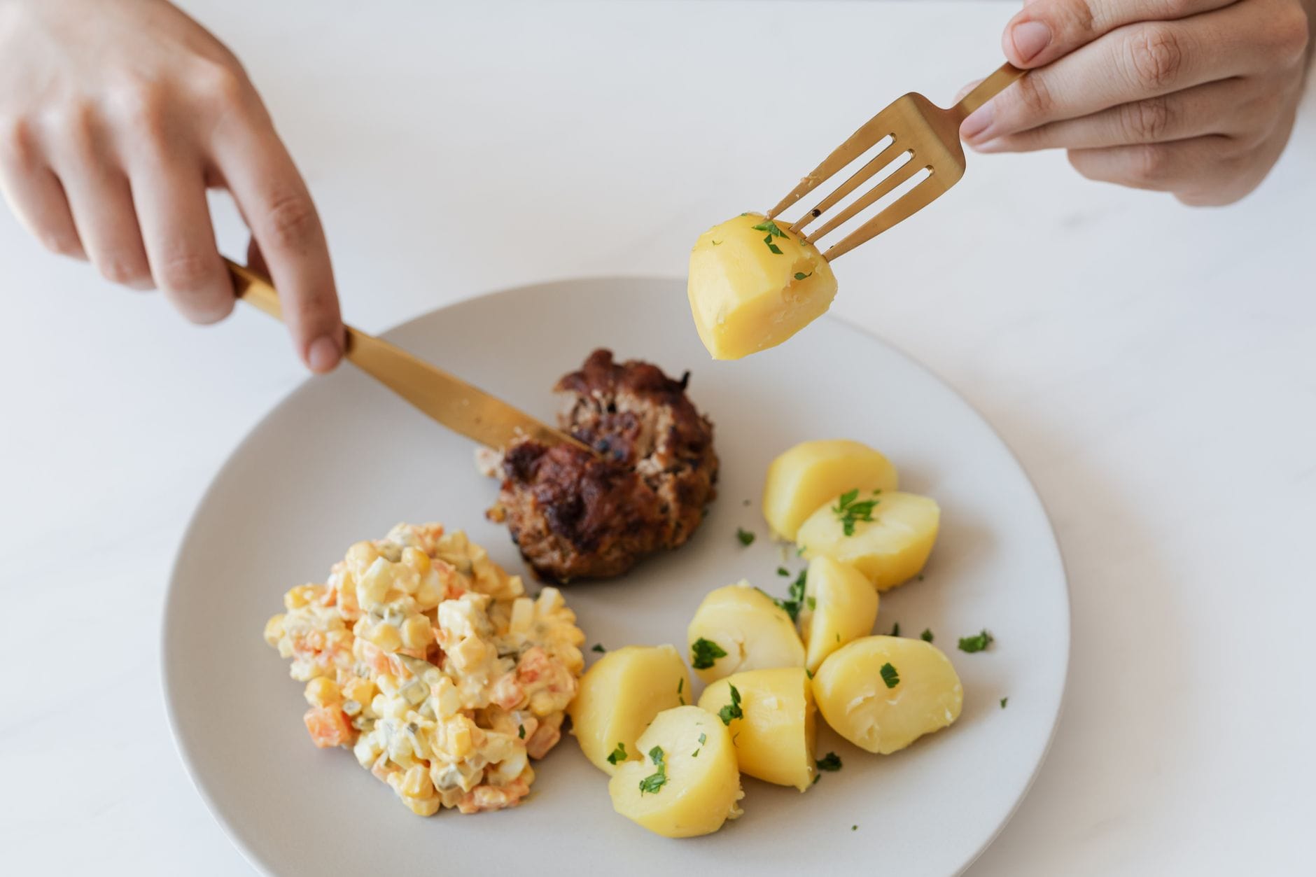 Talerz z kotletem, ziemniakami i sałatką w rękach osoby przy stole