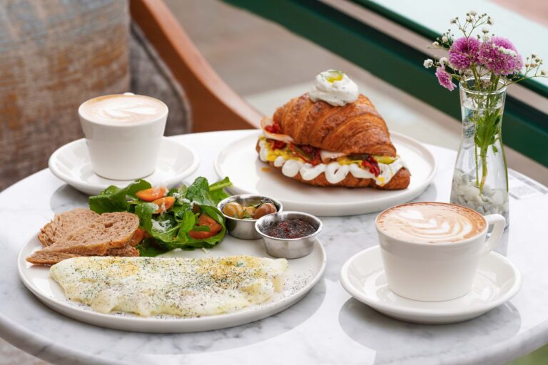 Latte, kanapka z croissantem, omlet i sałatka na marmurowym stole